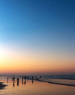 Silhouette people on beach against clear sky during sunset