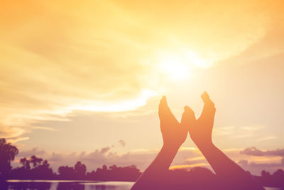 Silhouette woman hand against sky during sunset