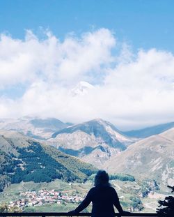 Rear view of woman looking at mountains against cloudy sky