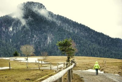 Rear view of child walking on dirt road against mountain during winter