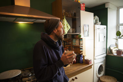 Thoughtful man holding cup in kitchen at home
