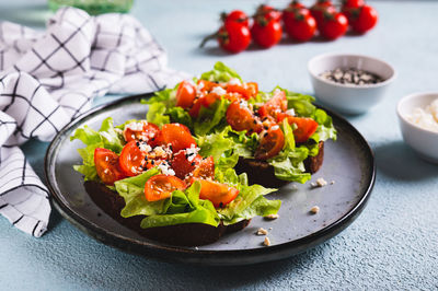 Bruschetta on rye bread with lettuce, tomatoes and sesame on a plate on the table