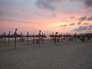 Thatched parasols on sand at beach against sky during sunset