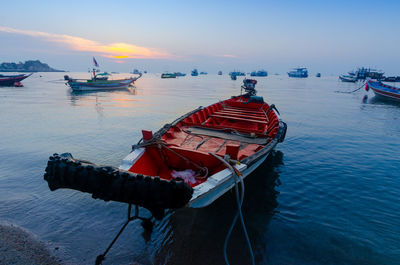 Fishing boat moored in sea against sky during sunset