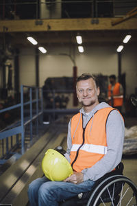 Portrait of smiling mature carpenter with hardhat sitting on wheelchair