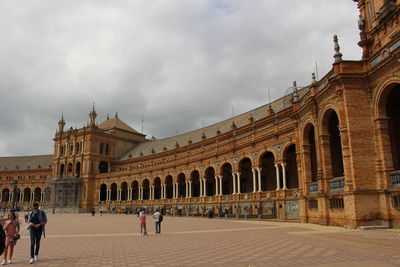 People in front of historical building against cloudy sky