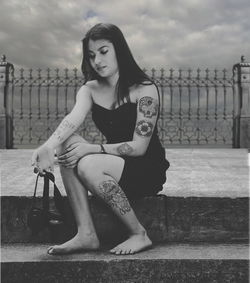 Young woman sitting on steps against cloudy sky