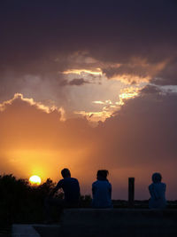 Silhouette people sitting against sky during sunset