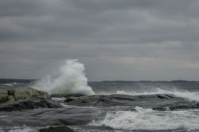 Waves splashing on rocks against sky