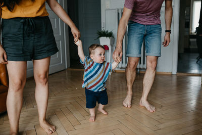 Low section of friends standing on floor at home