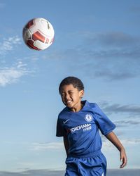 Smiling boy playing with ball in background against sky