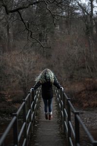 Rear view of woman walking on footbridge in forest