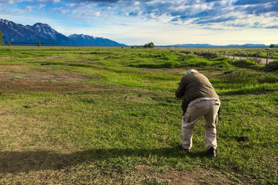 Rear view of man standing on grassy field against mountains