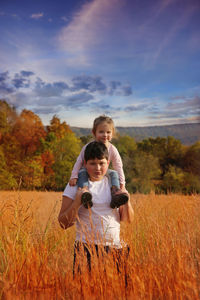 Happy brother with sister on field against sky