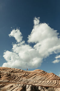 Blue cloudy skies and one hiker on top of petrified sand dunes of utah