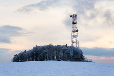 Communications tower on snow covered land against sky