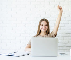 Mid adult woman using laptop on table against wall