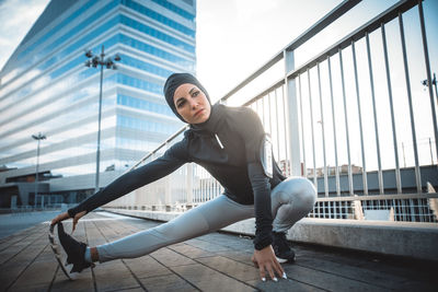 Full length of woman exercising on road against sky in city