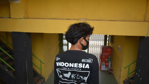 Rear view of woman standing against yellow wall