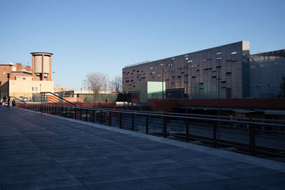 Footpath by buildings against clear blue sky