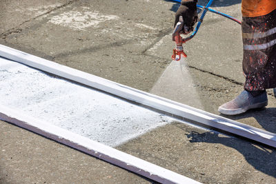 A road worker applies white road markings to a pedestrian crossing.