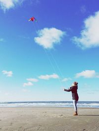 Woman flying kite at beach against sky