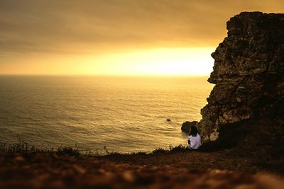 Silhouette people on rock by sea against sky during sunset