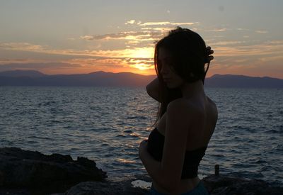 Side view of young woman standing at beach during sunset