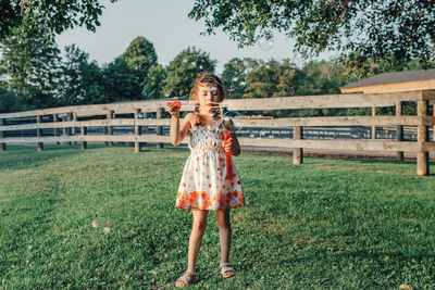 Full length of girl blowing bubbles while standing on field