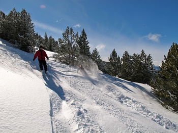 Men skiing downhill against sky on sunny day