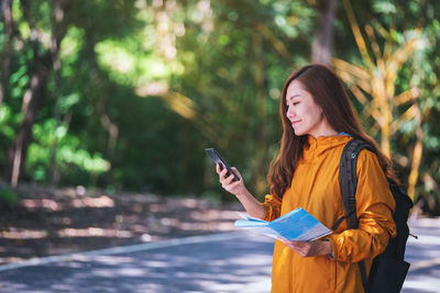 Smiling woman using mobile phone while holding map