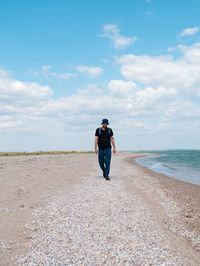 Bearded millennial man in bucket hat walking on empty beach. authentic hipster  outdoor solo travel 