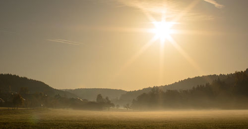 Sunlight streaming through trees on field against sky during sunset