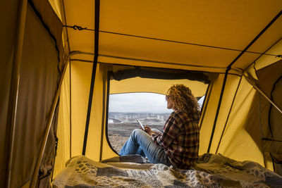 Side view of woman using phone while sitting in tent