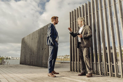 Two businessmen standing on jetty at a lake talking