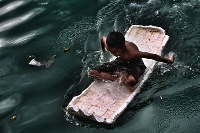 High angle view of shirtless boy sitting on raft at lake