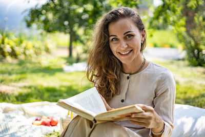 Portrait of young woman reading book while sitting outdoors
