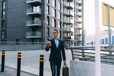 Businessman with briefcase using mobile phone while walking in city