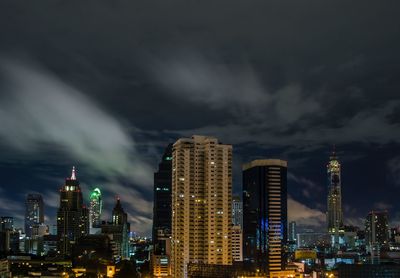 Illuminated buildings in city against storm clouds at night