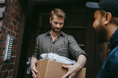 Mature man receiving parcel from courier delivery person while standing at doorstep