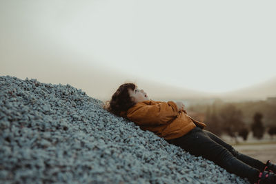 Side view of child lying down on land against sky