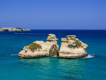 Scenic view of rocks in sea against clear blue sky