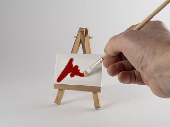 A male hand paints a canvas on the miniature easel