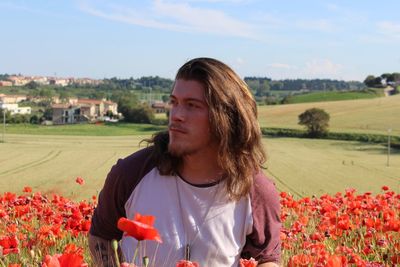 Young man looking away standing amidst flowers