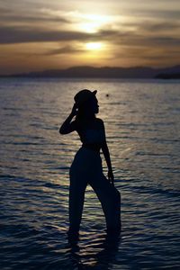 Silhouette woman in sea against sky during sunset