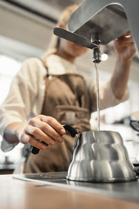 Female barista pouring boiling water in coffee pot from machine at counter in cafe