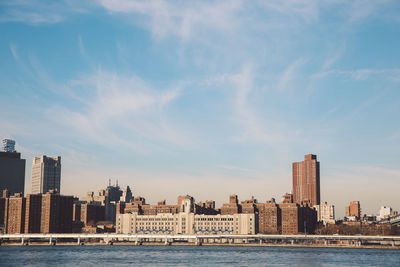 View of city at waterfront against cloudy sky