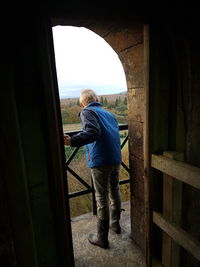 Rear view of boy standing in balcony seen through doorway