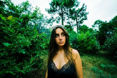 Portrait of beautiful young woman standing against trees
