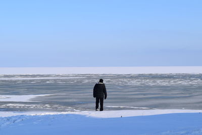 Rear view of man walking on frozen lake against sky